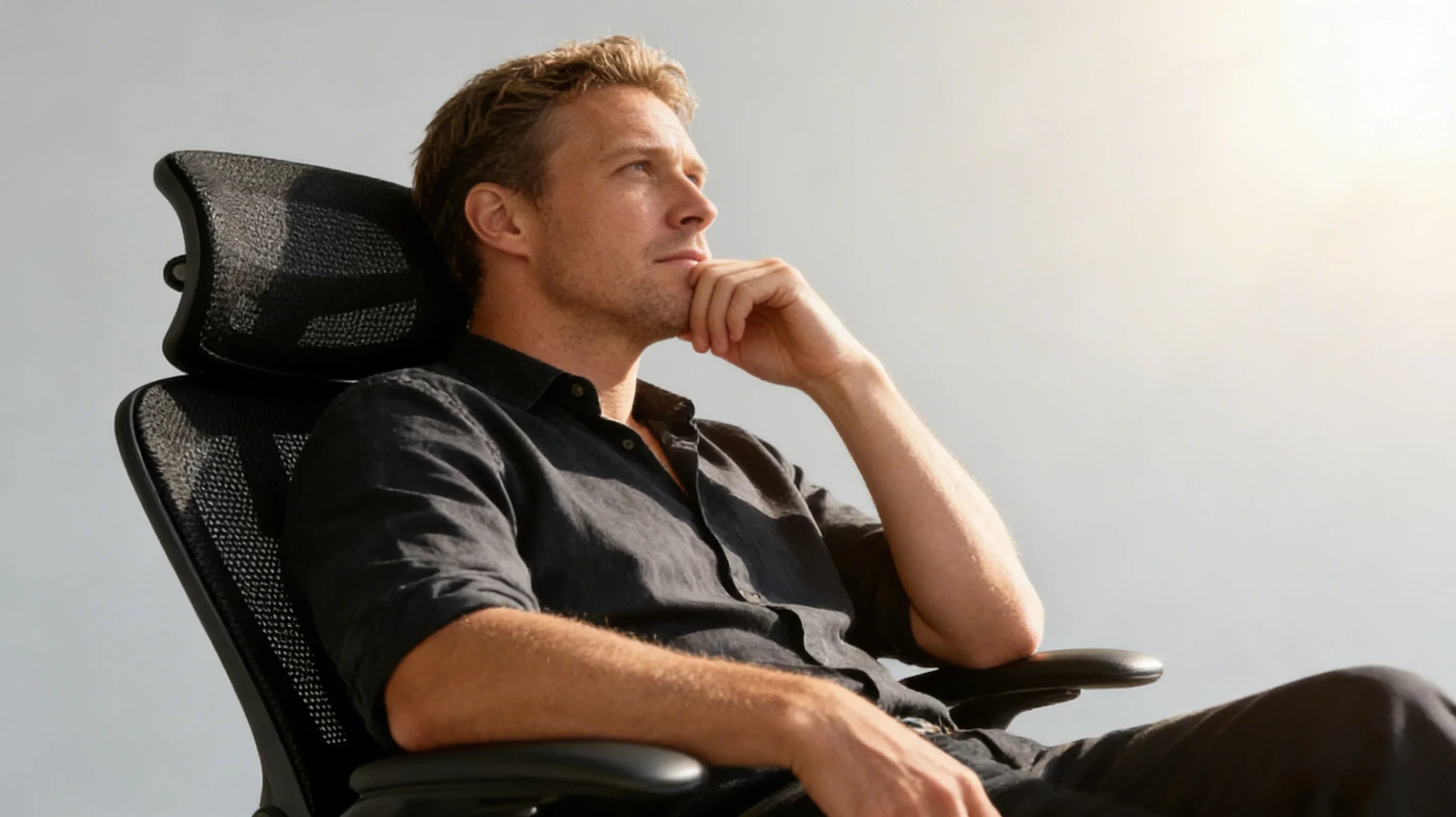 A minimalist interior designer in Copenhagen sitting in a sleek black ergo office chair.