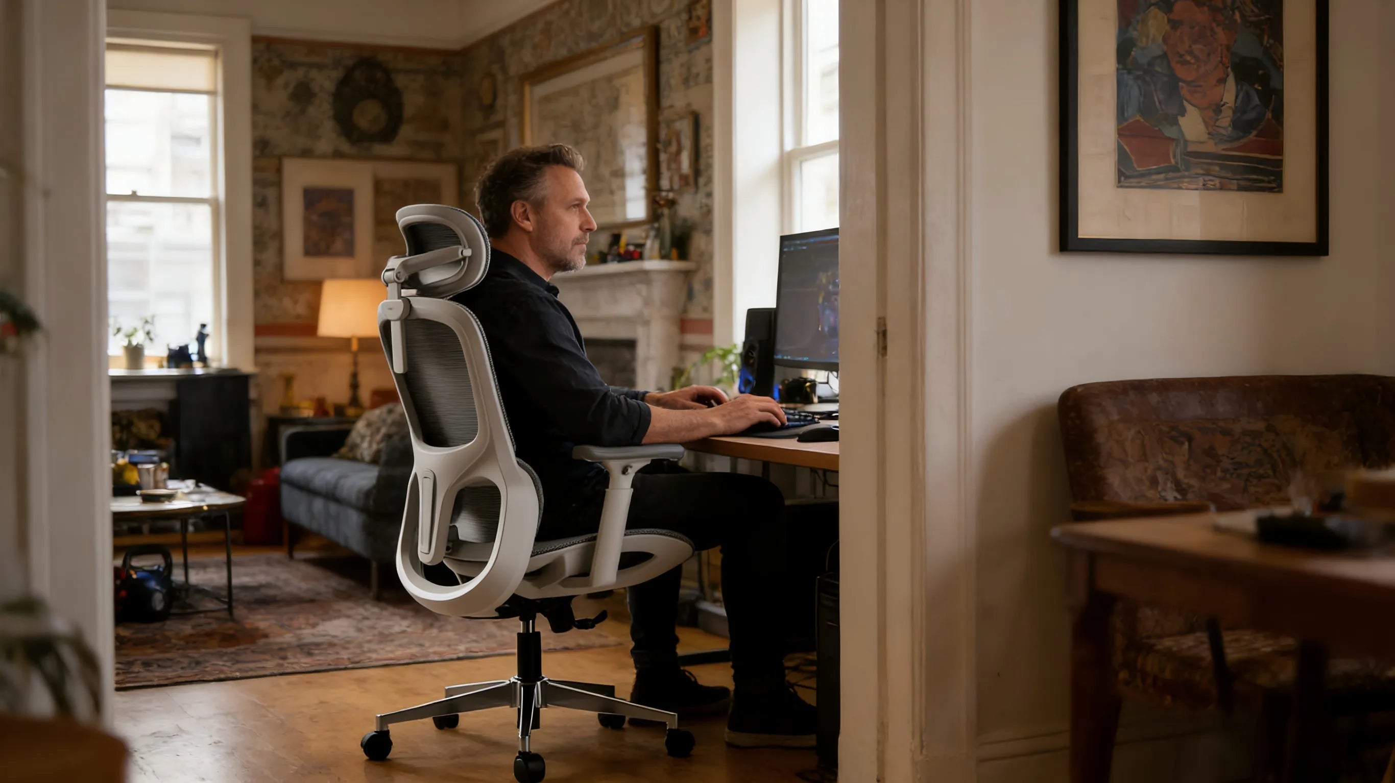 A casual gamer in a minimalist London studio using a white-framed video game chair at a dual-monitor setup.